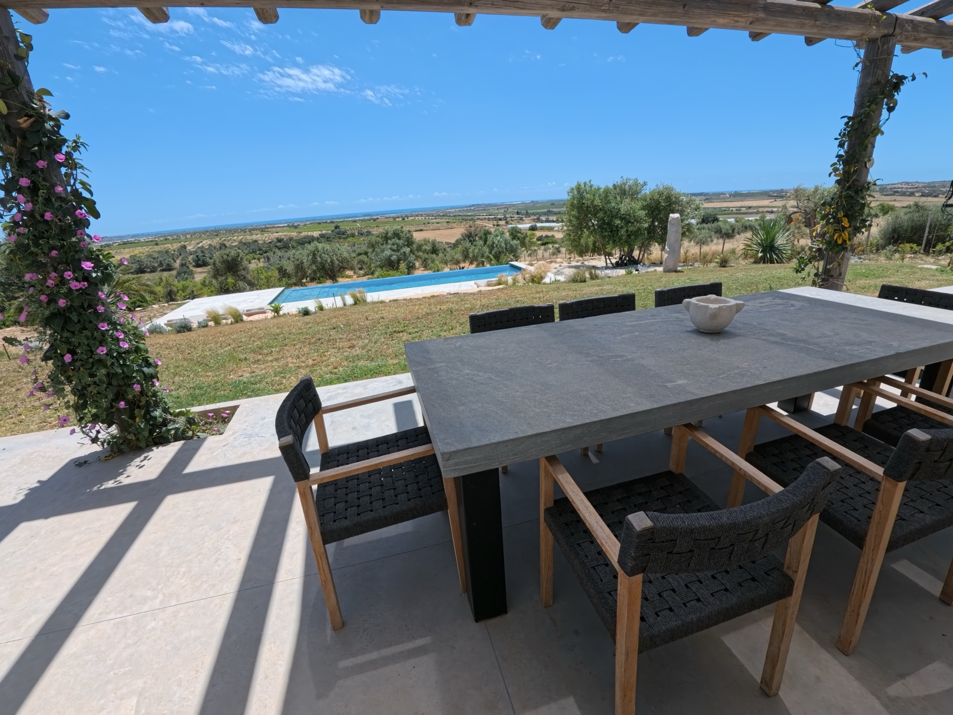 Outdoor dining under the pergola with bougainvillea, pool and countryside beyond